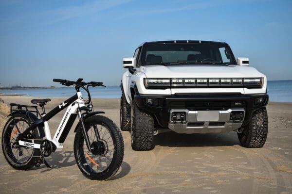 GMC Hummer EV Pickup Truck parked on a beach next to a GMC Hummer EV AWD EBike
