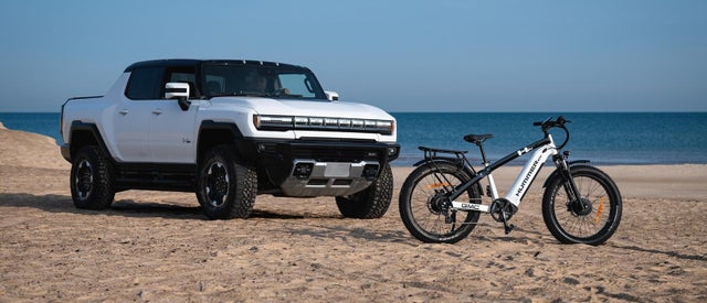 GMC Hummer EV Pickup Truck parked on a beach next to a GMC Hummer EV AWD EBike
